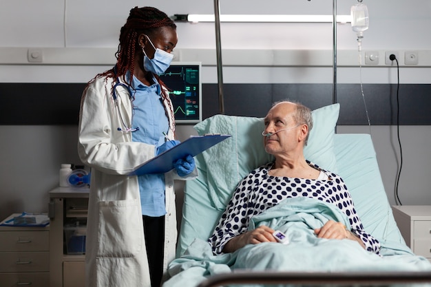 African american doctor with surgical mask reading diagnosis from clipboard