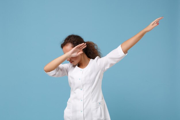 African american doctor woman isolated on blue background in\
studio. female doctor in white medical gown showing dab dance\
gesture. healthcare personnel health medicine concept. mock up copy\
space.