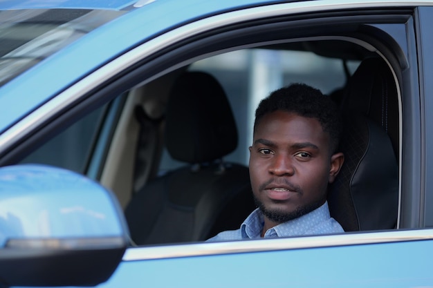 African american driver sits in black cabin of blue car