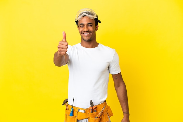 African American electrician man over isolated yellow wall with thumbs up because something good has happened