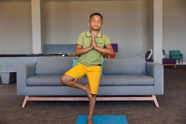 African american elementary boy with closed eyes standing on one leg while exercising in school