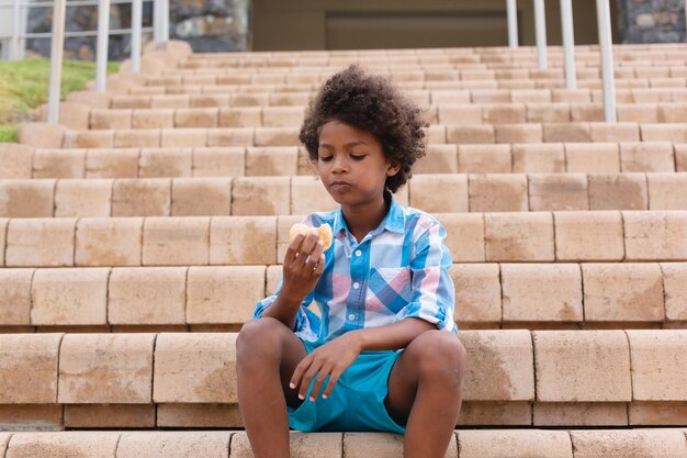 校舎の階段に座りながら食べ物を食べるアフリカ系アメリカ人の小学生