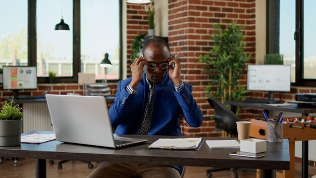 African american employee taking notes on documents and laptop, working on startup project. executive manager writing data report on computer, typing email on website browser app.