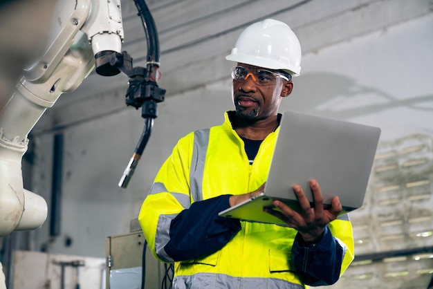 Афроамериканский фабричный рабочий, работающий с искусной роботизированной рукой