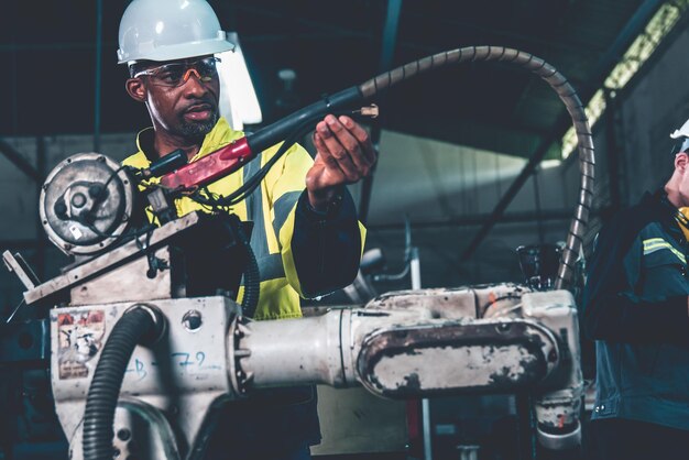 Афроамериканский фабричный рабочий, работающий с искусной роботизированной рукой