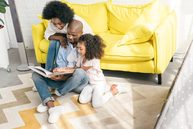 Photo african american family reading book together at home