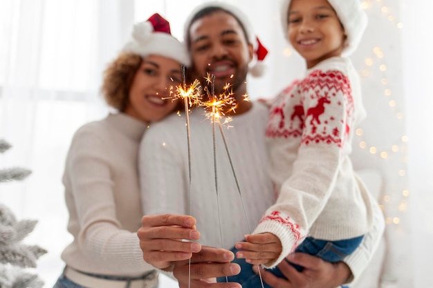 Foto famiglia afroamericana in cappelli di babbo natale celebra il capodanno con un bambino a casa e fuoco a scintillanti