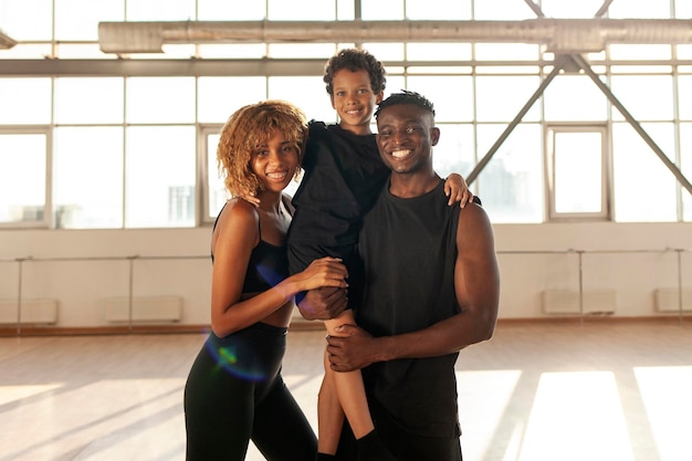 Афроамериканская семья в спортивной одежде стоит в спортзале и улыбается спортивным родителям со своим сыном