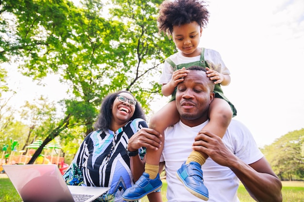 Padre afroamericano che dà al figlio un giro sulla schiena al parco la famiglia che gioca insieme e si rilassa