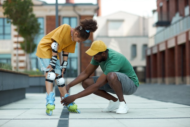 African american father helping his daughter to wear roller skates during their walk outdoors