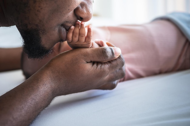 An African American father kissing hand his baby newborn daughter lying in white bed with happy