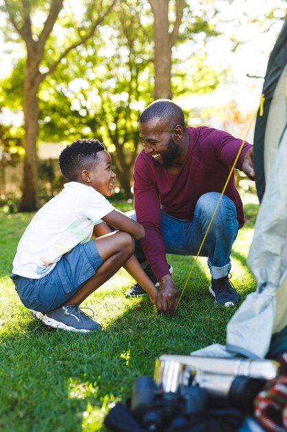 Photo african american father with son having fun and pitching tent in garden