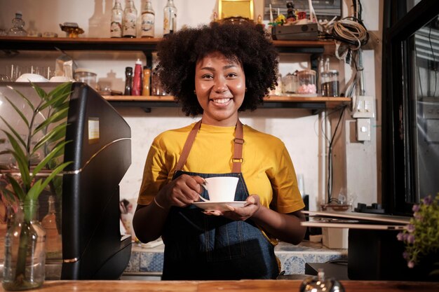 African American female barista cheerful offers a cup of coffee in casual cafe