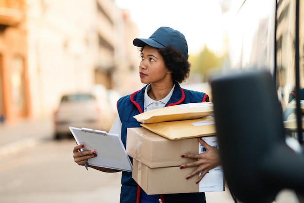 Consegnatore femminile afroamericano con i pacchetti che camminano per la strada