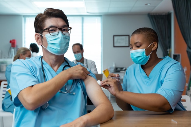 African american female doctor giving covid vaccination to male colleague, both in face masks