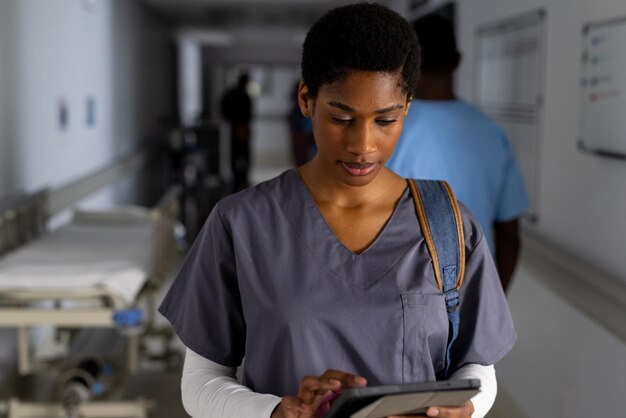 Photo african american female doctor using tablet in corridor at hospital