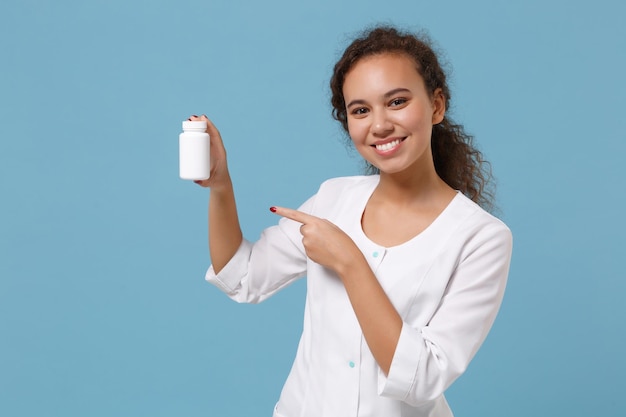 African american female doctor woman in medical gown point finger on medication tablets, aspirin pills in bottle isolated on blue background. Healthcare personnel medicine concept. Mock up copy space.