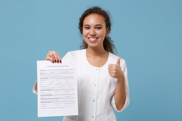 African american female doctor woman in medical gown showing\
thumb up, holding patient registration form isolated on blue\
background. healthcare personnel medicine health concept. mock up\
copy space.