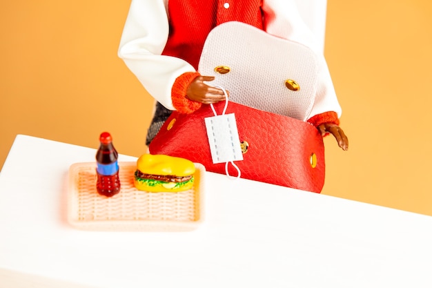 African-american female doll hand hold mask next to fastfood on a table