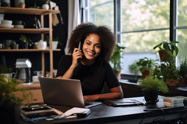 African American Female entrepreneur talking over mobile phone and looking at camera while working over laptop at home