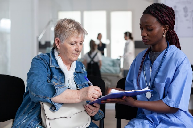 Photo african american female geriatrician discharging elderly patient from clinic. senior woman forming hospital discharge papers. sick old lady filling out files in hospital waiting room.