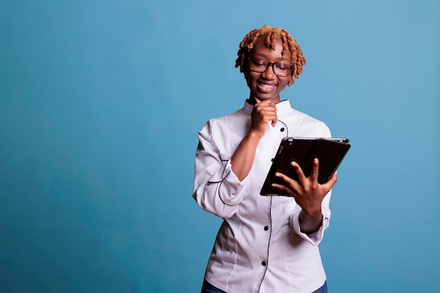 Lavoratrice di cucina afroamericana che guarda video di ricette sullo schermo del tablet. chef afro sorridente durante la video lezione di lavoro su dispositivo elettronico. cuoco della donna che si diverte con la tecnologia.