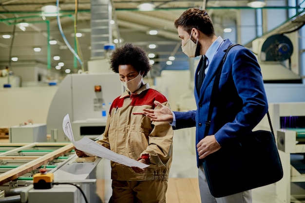 african american female worker and company manager examining blueprints at woodworking factory