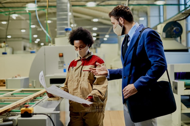 African American female worker and company manager examining blueprints at woodworking factory