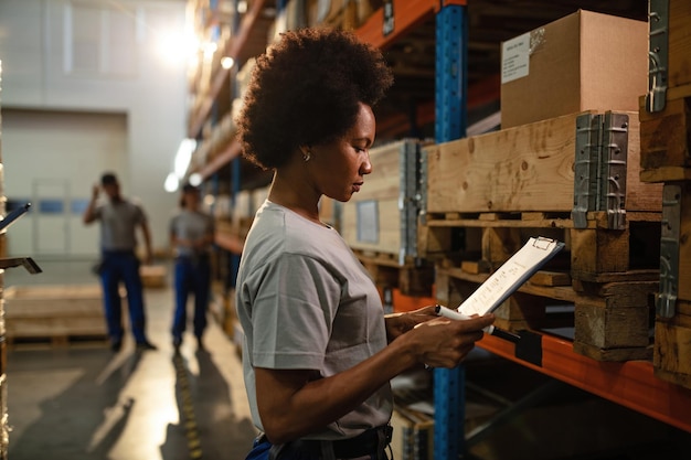 Foto lavoratrice afroamericana che legge l'elenco del programma di consegna mentre lavora nel magazzino di distribuzione