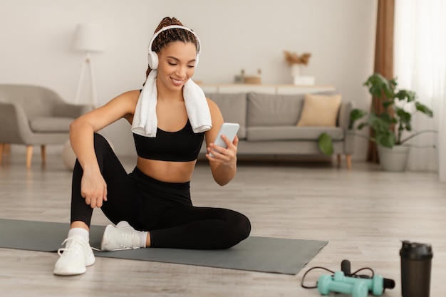 African american fitness woman using smartphone exercising wearing headphones indoor