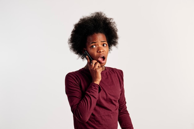갈색 스웨터를 입은 아프리카계 미국인 소녀가 전화 통화를 하는 동안 포즈를 취합니다.