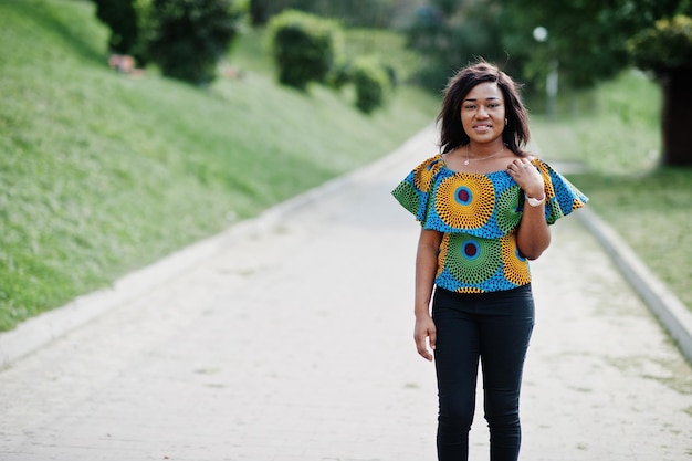 Ragazza afroamericana in camicia colorata e pantaloni neri poste all'aperto donna nera alla moda