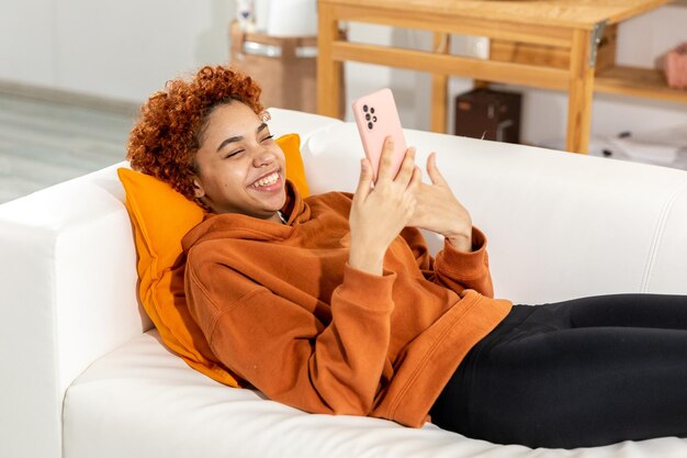 African american girl lying on couch with smartphone having video chat female blogger chatting with