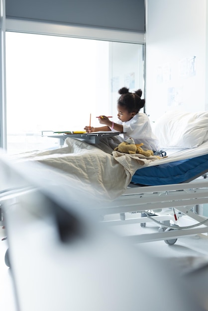 사진 아프리카계 미국인 소녀 환자가 병원의 환자실에서 침대에 누워서 색을 칠하고 있습니다. 병원, 유년기, 의학 및 의료, 변하지 않습니다.
