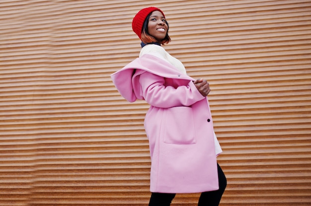 African american girl in red hat and pink coat against orange shutters.