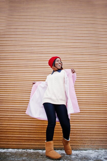 African american girl in red hat and pink coat against orange shutters