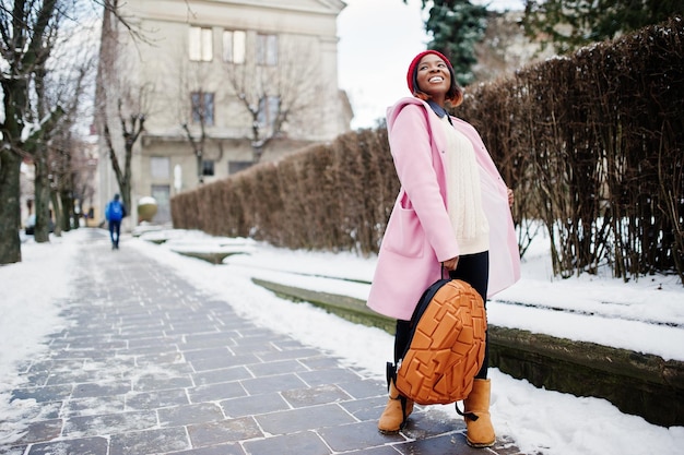 African american girl in red hat and pink coat with backpack at street of city on winter day