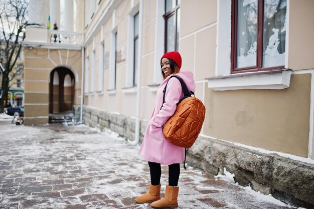 African american girl in red hat and pink coat with backpack at\
street of city on winter day