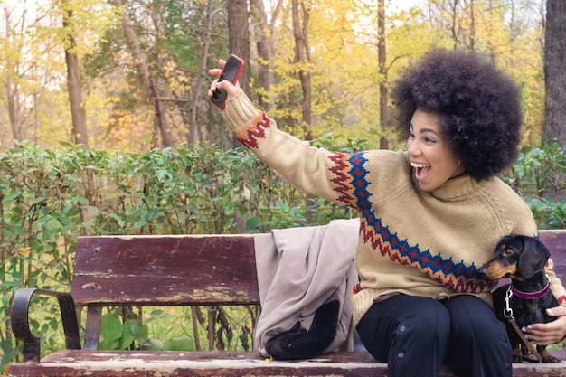 An african american girl sitting on a bench with her dachshund calling her friends