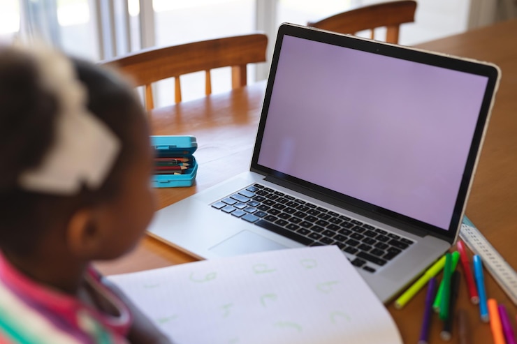 Photo african american girl sitting at dining table with pens and book, using laptop, copy space on screen