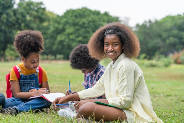 African American girl sitting and doing homework with her friends in the park of school. Education outdoor concept