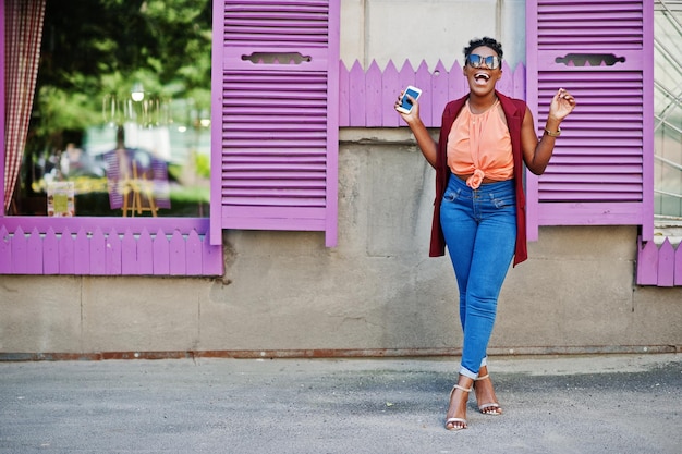 African american girl in sunglasses posed against purple windows with cell phone at hand