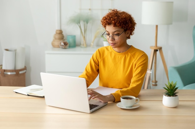 African american girl using laptop at home office looking at screen typing chatting reading writing