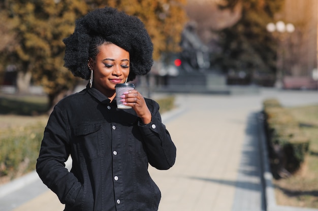 アフリカ系アメリカ人の女の子がコーヒーを飲みながらその場所を歩きます