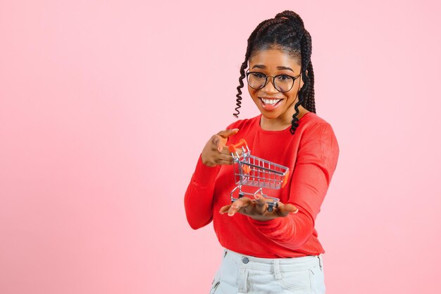 African american girl with shopping cart on pink background The concept of profitable sales or purchases