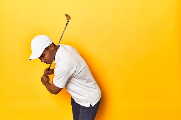 African American golfer in action posed in a yellow background studio