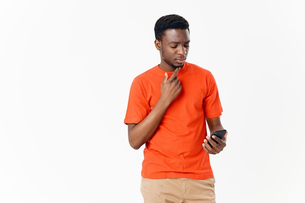 African American guy in an orange Tshirt with a mobile phone on a light background