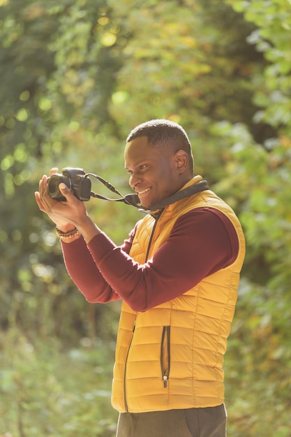 African american guy photographer taking picture with photo camera on city green park leisure activity diversity and hobby concept