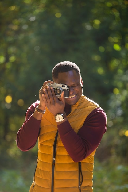 African american guy photographer taking picture with vintage camera on city green park leisure activity diversity and hobby concept