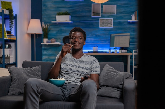 African american guy resting on sofa watching comedy movie on television